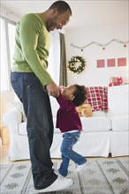 Black father and daughter dancing in living room