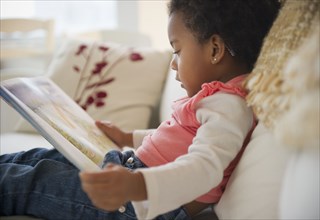 Black girl reading book on sofa