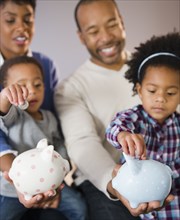 Black parents watching children put money in piggy bank