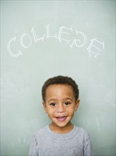 Black boy standing underneath the word college on blackboard