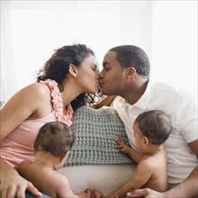 Parents kissing on sofa next to twin baby boys