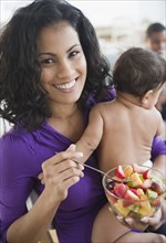 Mother holding baby and eating fruit salad