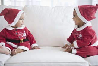 Twins on sofa dressed in Santa outfits