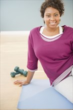 African woman sitting on yoga mat with dumbbells