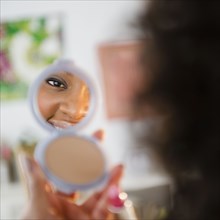 African American woman looking at reflection in compact