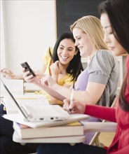 Women studying and looking at cell phone together in classroom