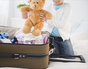 African American girl putting teddy bear in suitcase