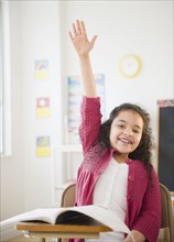 Hispanic girl raising hand in classroom