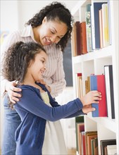 Mother helping daughter choose book on shelf