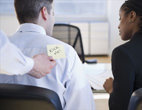 Businessman putting "kick me" sign on co-workers back