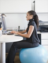 African American woman sitting on exercise ball at desk