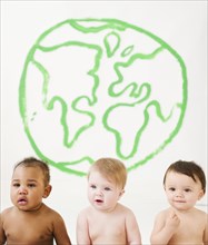 Babies sitting together with drawing of globe on wall