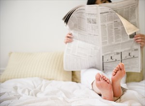 Korean woman reading newspaper in bed