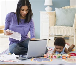 African American mother working on laptop while baby plays on floor