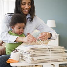 African American mother holding baby on lap and tying newspapers