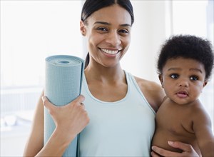 African American mother holding baby boy and yoga mat