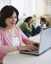 Woman using laptop with family in background