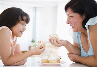 Hispanic mother and daughter eating cupcakes