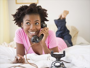 Black woman laying in bed talking on old-fashioned telephone