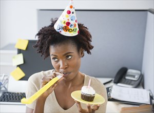 Black businesswoman blowing party blower at desk