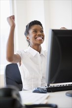 Excited Black businesswoman cheering at desk
