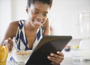 Black woman using digital tablet and eating cereal