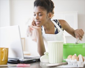Black woman cooking and looking at recipe on laptop