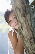 Hispanic girl hiding behind tree