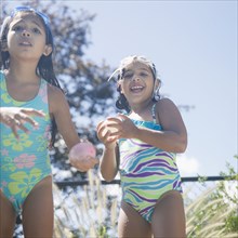 Hispanic girls in bathing suits playing with water balloons