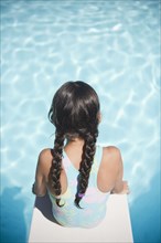 Hispanic girl sitting on diving board over swimming pool