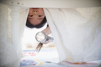 Korean girl looking under bed with flashlight