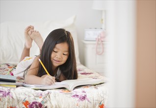 Korean girl doing homework on bed