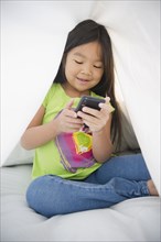 Korean girl using cell phone under sheet