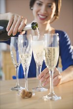 Mixed race woman pouring Champagne into glasses