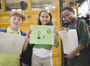 Children holding drawings near school bus