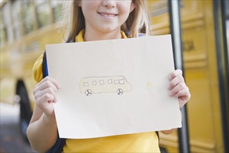 Caucasian girl holding drawing of school bus