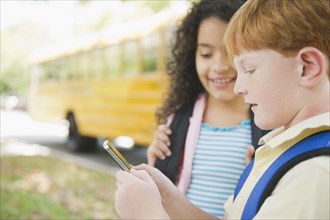 Children using cell phone while waiting for school bus