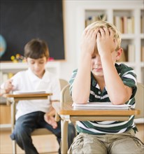 Frustrated Caucasian boy sitting at desk in classroom