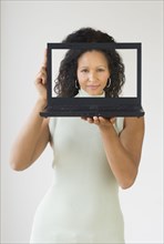 Hispanic woman holding laptop in front of her face