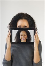 Hispanic woman holding digital tablet in front of face