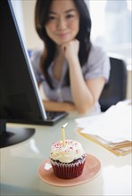 Birthday cupcake on desk near Japanese businesswoman