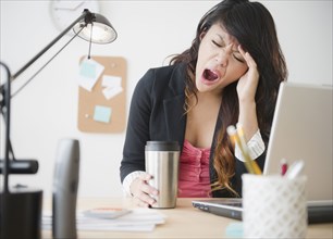 Pacific Islander businesswoman yawning at desk