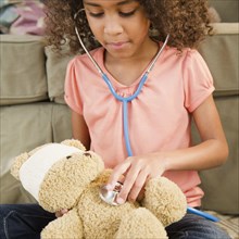 Mixed race girl using stethoscope on teddy bear