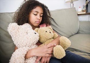 Mixed race girl sitting on sofa with teddy bear