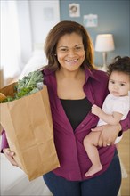Mixed race mother holding groceries and baby