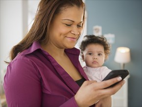 Mixed race mother holding baby and text messaging on cell phone