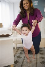 Mixed race woman helping baby learn to walk