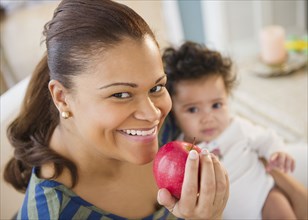 Mixed race mother holding baby and eating apple