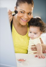 Mixed race other holding baby and putting on makeup