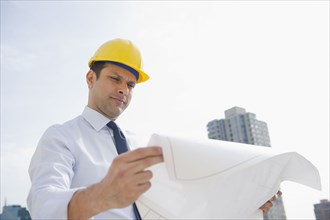 Mixed race businessman looking at blueprints on construction site